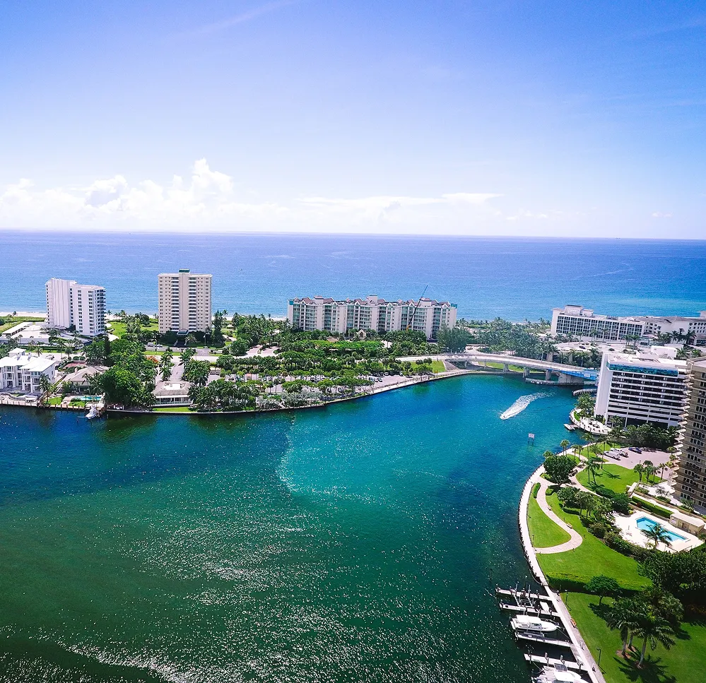Aerial view of a coastal resort with turquoise water, buildings along the shoreline, and a marina.