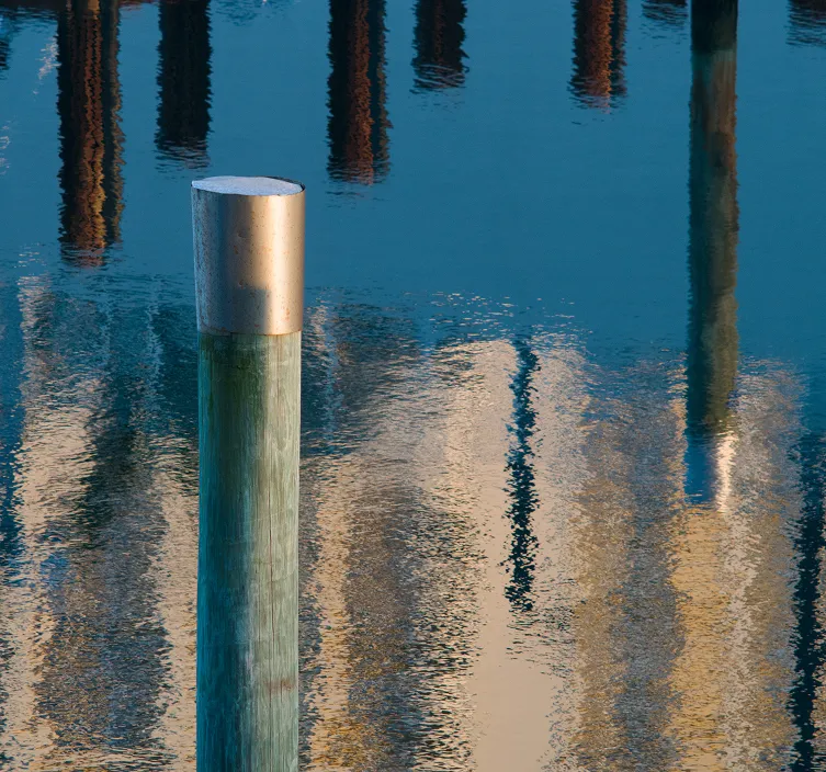A weathered green dock post with a silver cap, reflected in calm water.