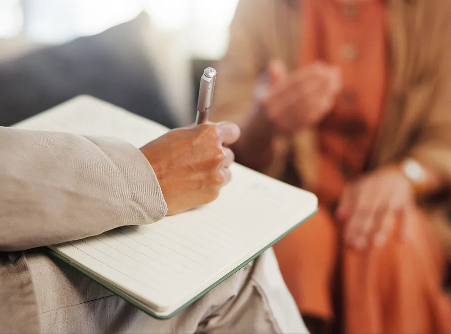 Person holding a pen and writing in a notebook during a discussion